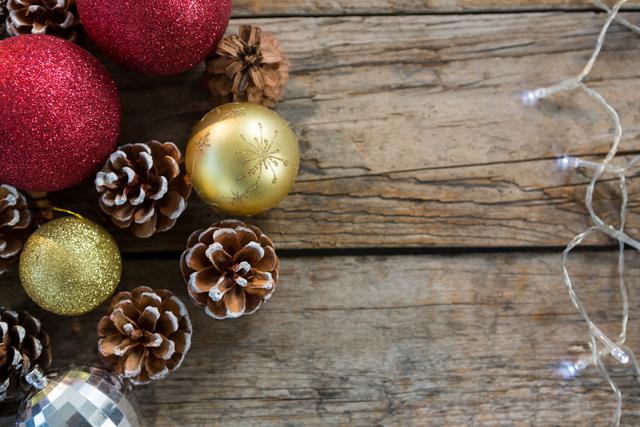 This image shows a collection of Christmas decorations, including glittery baubles and pine cones, arranged on a rustic wooden table. It is perfect for holiday-themed projects, festive greeting cards, seasonal advertisements, and social media posts celebrating Christmas.