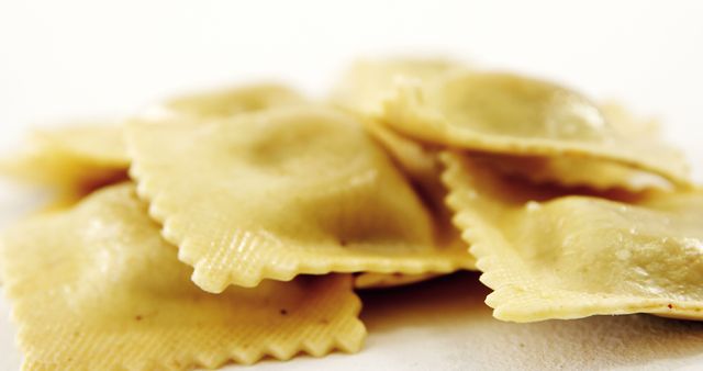 High-resolution close-up shows fresh, uncooked ravioli pasta piled on a white surface. Details of the pasta texture and shape are clearly visible, making it perfect for culinary blogs, cooking magazines, business promotions for Italian restaurants, and food packaging designs.