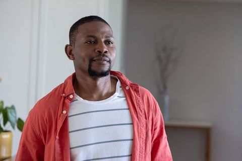 Contemplative african american man standing and looking right in minimalist modern living room