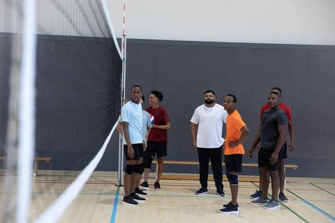 Diverse men preparing for indoor volleyball match at net with ball and knee pads