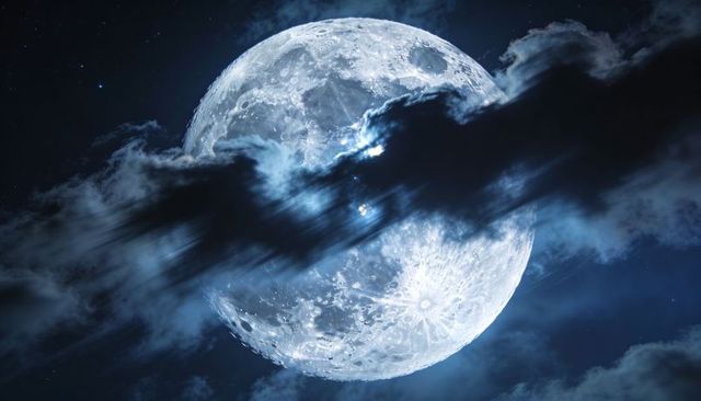 Full moon breaking through fast-moving clouds with luminous craters and starry sky