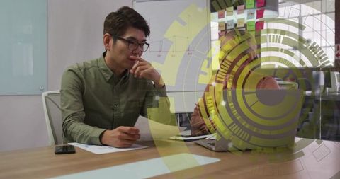 Asian man and woman wearing headscarf reviewing documents and typing on laptop