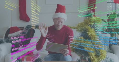 Man wearing santa hat waving while using tablet with festive augmented reality code overlay