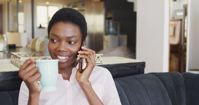 Woman holding cup smiling and talking on phone, ideal for illustrating relaxed communication, leisure time at home, modern interior lifestyle, and casual family or personal moments.