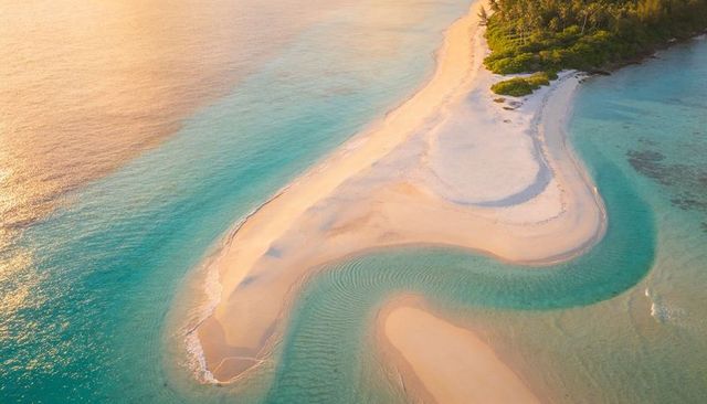 Aerial sandbar curving through turquoise lagoon at golden hour on tropical island coastline