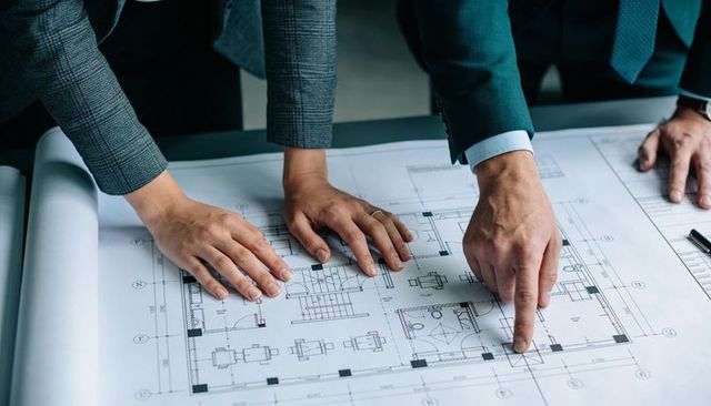 Architects reviewing office floor plan blueprint pointing and tracing layout collaborating