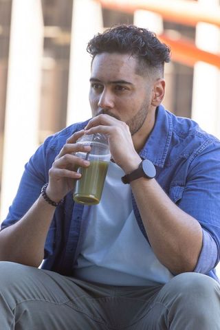 African american man sipping green smoothie on city steps in denim and smartwatch
