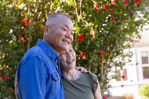 Senior couple embracing and smiling in sunny garden with red camellia blooms