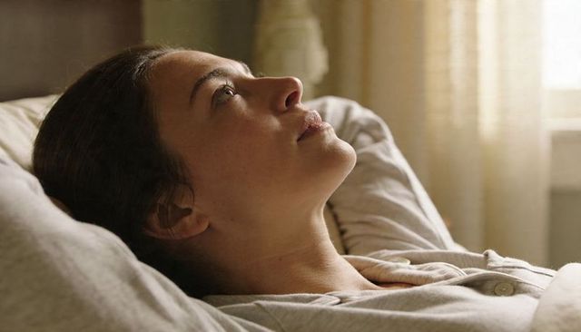 Serene woman reclining on pillow in soft morning light, gazing toward window, relaxing