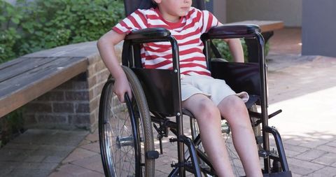 Child using manual wheelchair on sunlit patio touching wheel showing mobility independence
