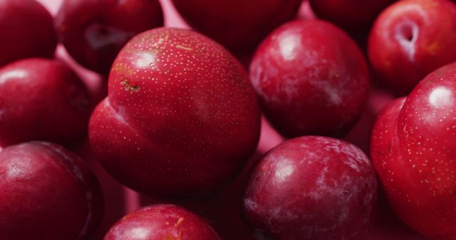 Close-up of fresh, vibrant red plums against a red background. Ideal for use in advertisements, grocery store displays, farmers market promotions, healthy eating blogs, and nutrition articles. Emphasizes freshness and natural food textures.