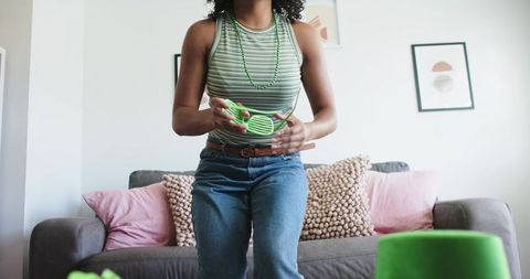 Young african american woman stacking bright green cups on sofa in playful at-home moment