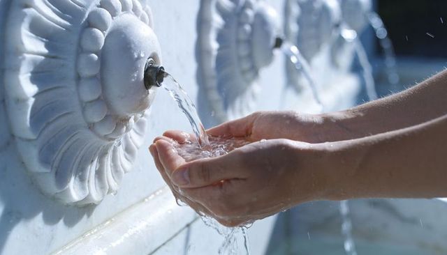 Cupping hands collecting cool water from ornamental marble fountain spout