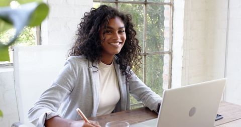 Smiling Woman Working at Home Office Desk with Laptop and Notebook