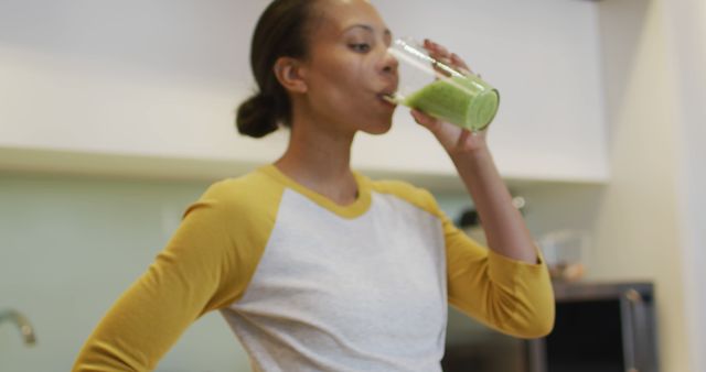 Biracial woman drinking healthy drink in kitchen. domestic life, spending quality free time relaxing at home.