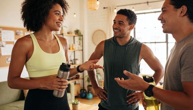 Sunlit home gym friends chatting smiling after workout holding water bottles kettlebell