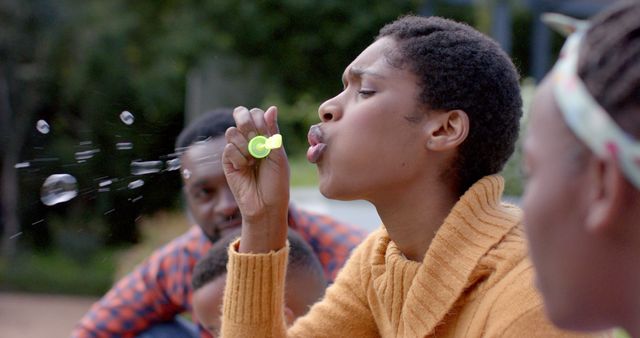 Happy african american parents, son and daughter blowing bubbles in garden. Family, childhood, spring, happiness, unaltered.