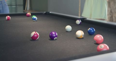 Friends leaning over black felt pool table watching colorful billiard balls scattered
