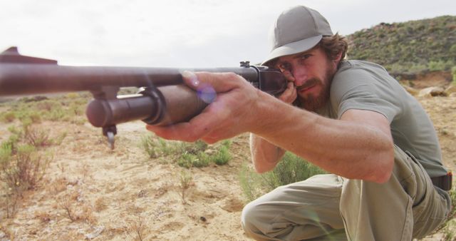 Kneeling caucasian male survivalist taking aim with hunting rifle in wilderness. exploration, travel and adventure, survivalist in nature.