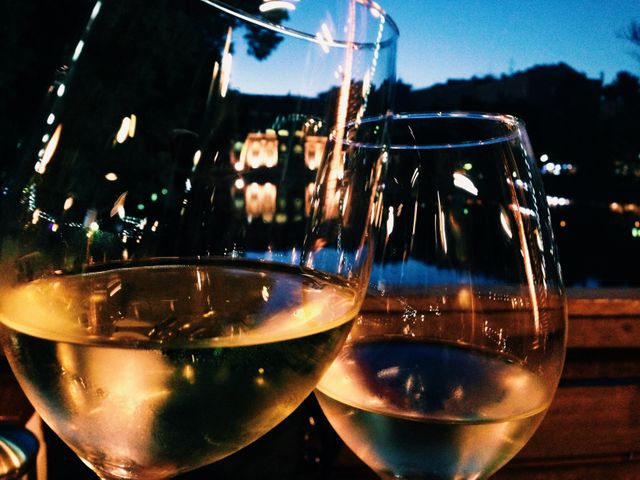 Two glasses of wine are clinking against each other with a background of blurred city lights and reflections on water at night. Ideal for use in articles, advertisements, or social media posts about celebrations, romantic dinner dates, urban nightlife, or fine dining experiences.