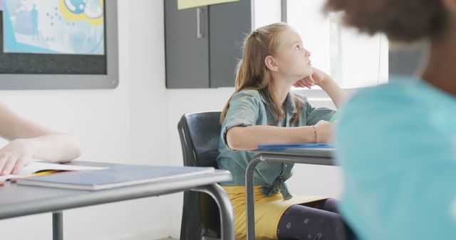 Image of bored caucasian schoolgirl sitting at desk looking out of window in class, copy space. Education, childhood, elementary school and learning concept.