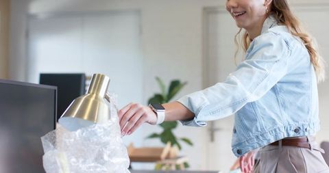 Young professional unpacking desk lamp and setting up modern minimalist office workspace
