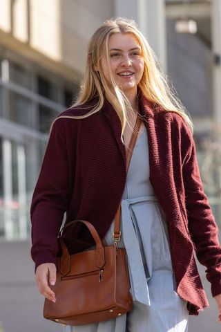 Sunlit young woman walking in city wearing maroon cardigan carrying leather handbag