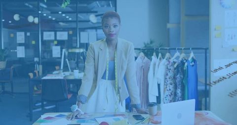 Female fashion designer leaning on table in creative studio with fabric swatches
