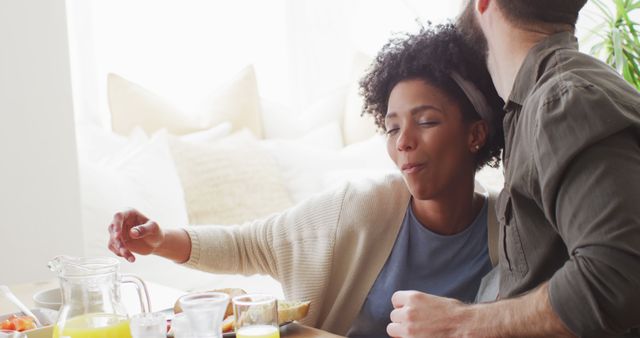 Image of happy diverse couple eating breakfast and talking at table. Happiness, inclusivity, free time, togetherness and domestic life.