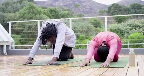 African American pair practicing restorative yoga on rooftop deck overlooking green hills