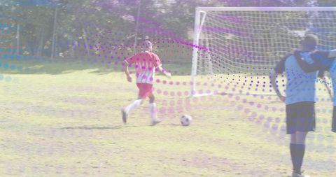 Youth soccer striker dribbling toward goal with keeper and teammates on sunlit park field