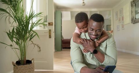 African american father and son bonding and sharing phone in sunlit living room