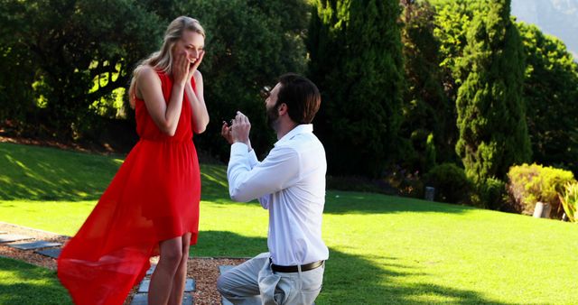 A man is proposing to a woman outdoors, with copy space. She appears surprised and joyful, capturing a significant moment in their relationship.