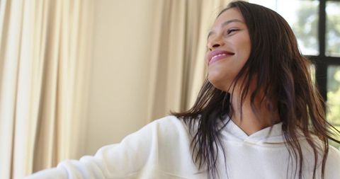 Young african american woman smiling gazing upward cozy white hoodie window natural light