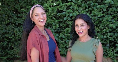 Laughing friends enjoying sunny garden moment with hoop earrings and casual outfits