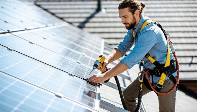 Rooftop Solar Technician Fastening Panel Clamp While Wearing Safety Harness and Lanyard
