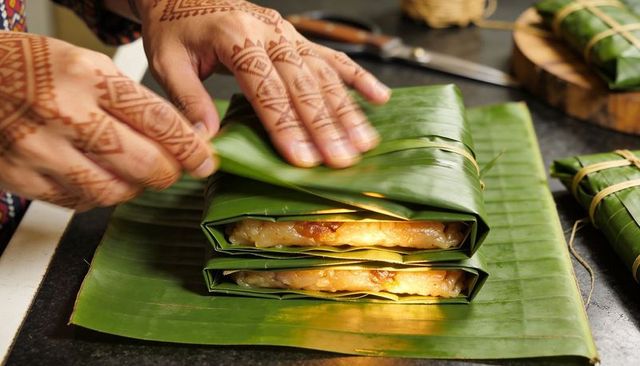 Hand-wrapping banana-leaf sticky rice parcels with henna-decorated hands close-up