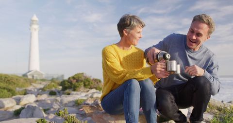 Joyful Senior Couple Enjoying Coffee by Seaside Lighthouse