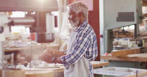 Seasoned Carpenter Dusting Hands in Sunlit Workshop