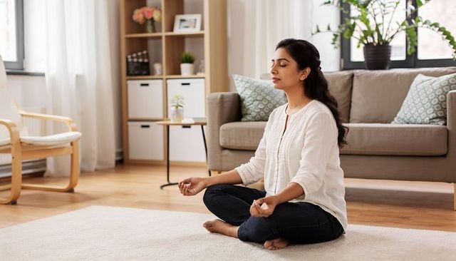Indian woman meditating at home in minimalist living room, calm mindful lifestyle