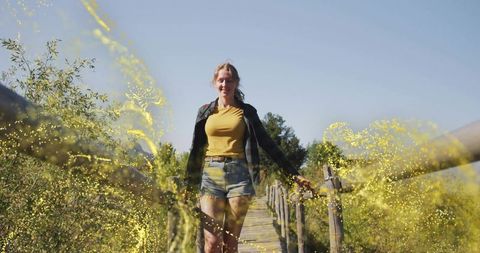 Woman in Mustard Attire Walking on Boardwalk with Golden Particles
