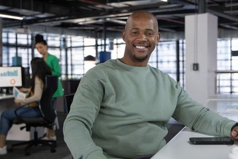 Smiling black professional working in modern open office with smartphone and team