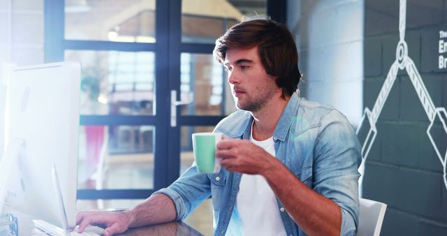 Young Man Drinking Coffee While Working on Desktop Computer in Modern Office - Download Free Stock Images Pikwizard.com