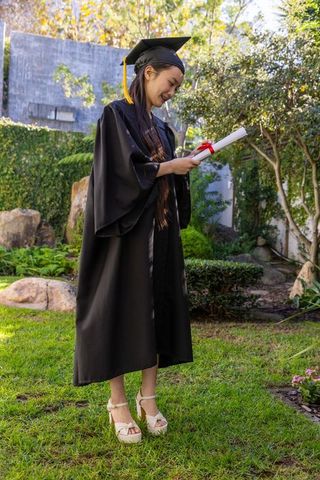 Graduating student celebrating milestone in graduation gown and cap outdoors