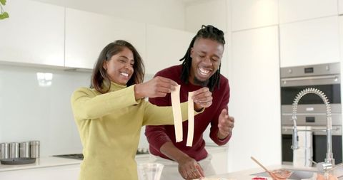 African american man and indian woman preparing fresh pasta ribbons in modern kitchen