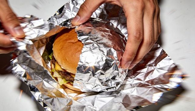 Hands unwrapping foil-wrapped cheeseburger with melting cheese and lettuce