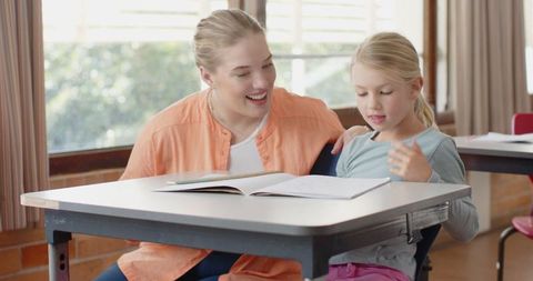 Mother encouraging daughter in learning with open workbook