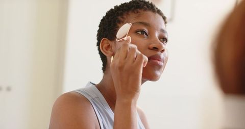 African woman applying rose quartz facial roller for glowing skin morning skincare ritual