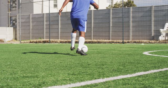 Midsection of biracial male football player wearing blue uniform training on outdoor pitch. Football, sports and fitness.