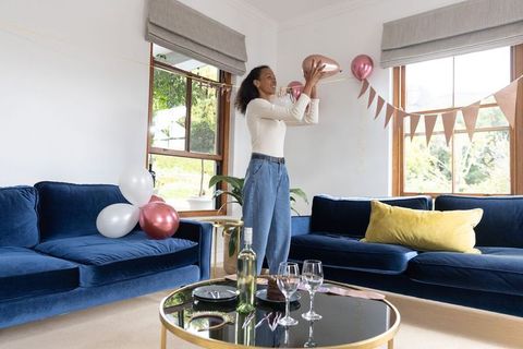 Woman decorating sunlit living room for intimate party with velvet sofas and balloons